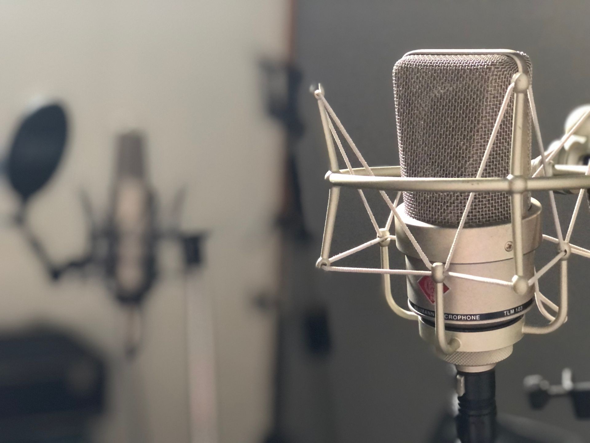 Close-up of a professional studio microphone with another microphone and equipment blurred in the background.