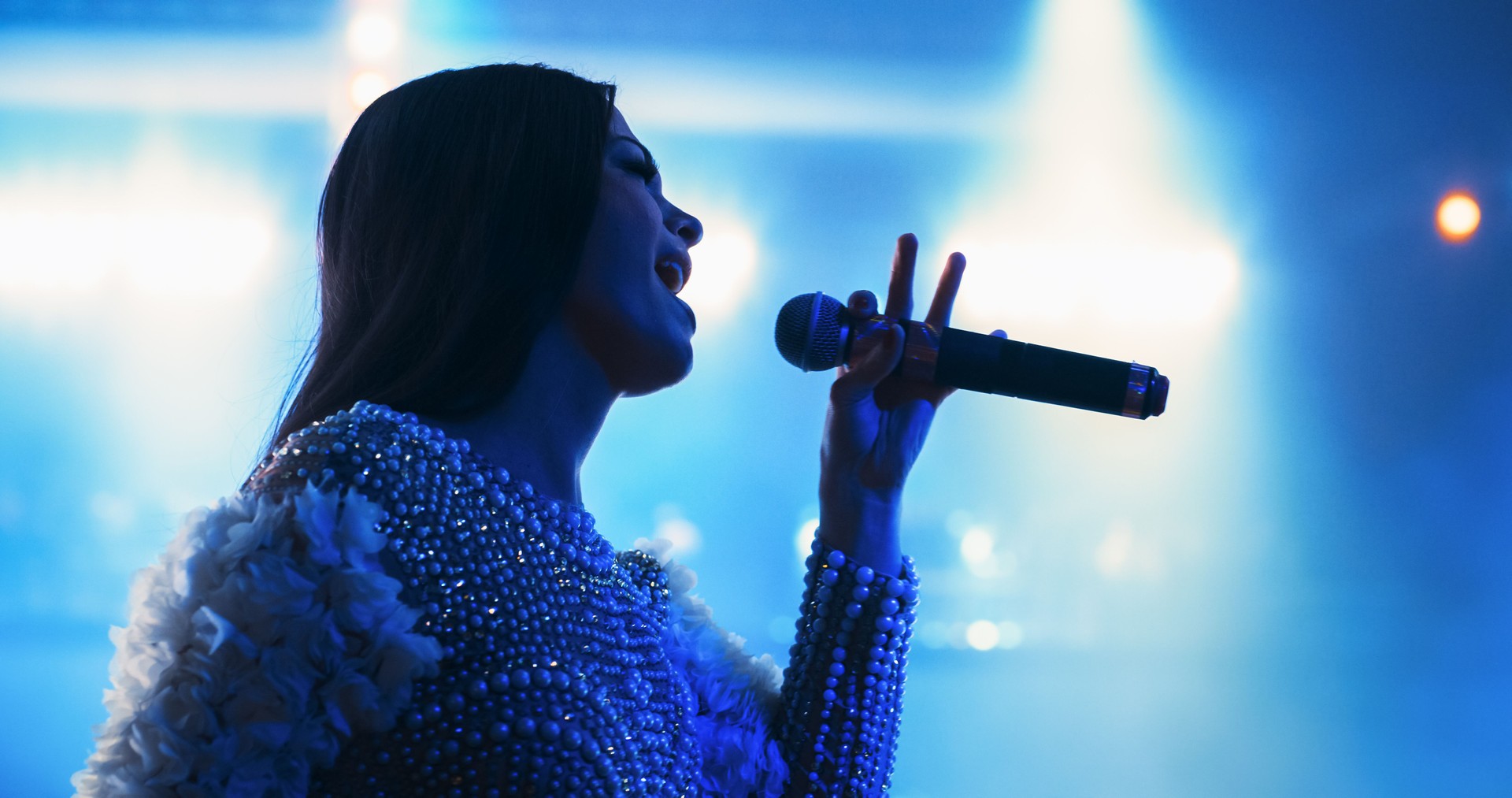 Female Pop Musician Performing Live Concert on Stage, Illuminated by a Spotlight. Epic Cinematic Performance Captures Artist's Passion and Energy. Dramatic Close Up on the Face